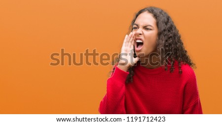 Young hispanic woman wearing red sweater shouting and screaming loud to side with hand on mouth. Communication concept.