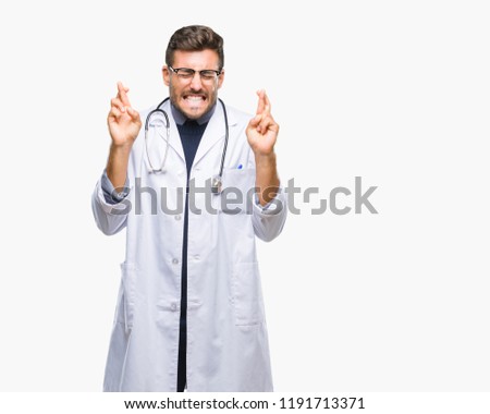 Young handsome doctor man over isolated background smiling crossing fingers with hope and eyes closed. Luck and superstitious concept.