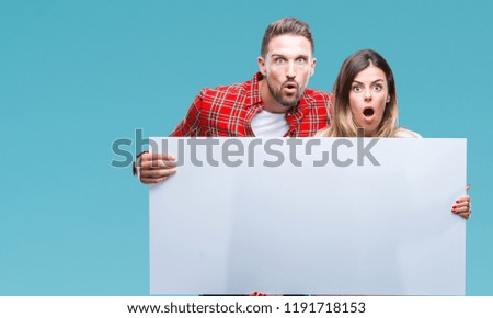 Young couple together holding blank banner over isolated background scared in shock with a surprise face, afraid and excited with fear expression