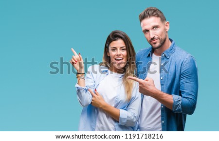 Young couple in love over isolated background with a big smile on face, pointing with hand and finger to the side looking at the camera.