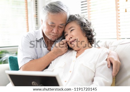 Sad frustrated mature old woman in tears feeling blue thinking of loneliness sorrow grief, husband comforting his upset wife together while sitting on sofa and looking at picture at home.