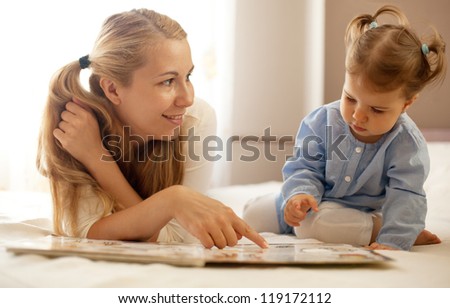 young mother and baby girl reading book together