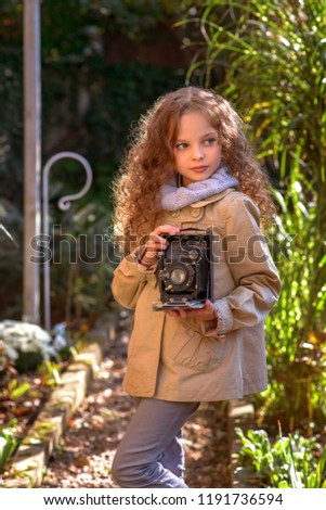 Portrait of young beautiful child with retro camera. Little girl with old photography camera in hands outdoors.