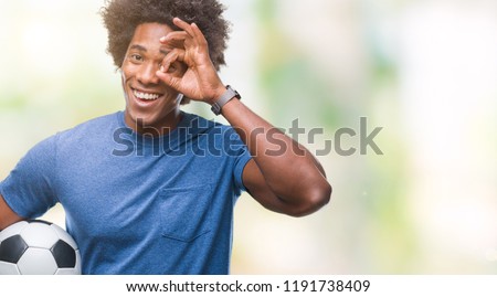 Afro american man holding football ball over isolated background with happy face smiling doing ok sign with hand on eye looking through fingers