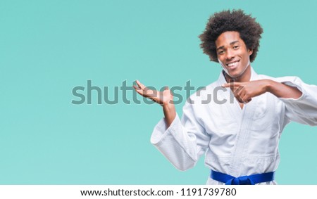 Afro american man wearing karate kimono over isolated background amazed and smiling to the camera while presenting with hand and pointing with finger.