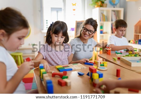 Preschool teacher with children playing with colorful wooden didactic toys at kindergarten Royalty-Free Stock Photo #1191771709