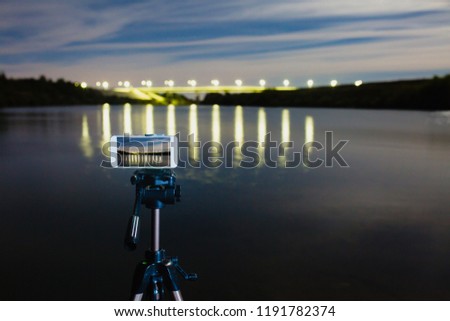 Using smartphone like professional camera on tripod to capturing night landscape with a lot of lights reflected on surface of the water