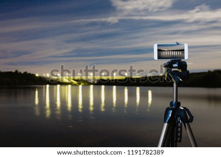 Using smartphone like professional camera on tripod to capturing night landscape with a lot of lights reflected on surface of the water