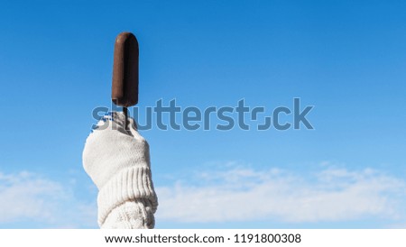 Female hand in knitted gloves with chocolate ice cream on the stick in the winter snowfall background. Concept
