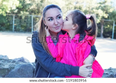 Cute little girl is kissing her mother in the park