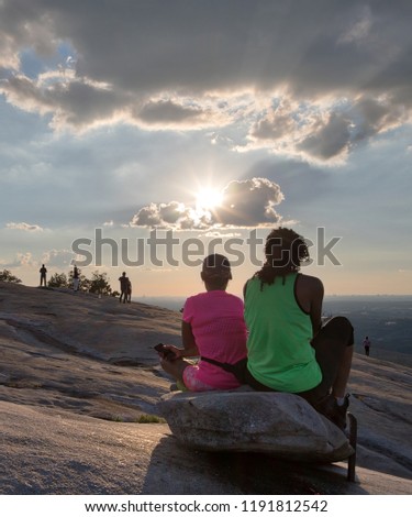 Unidentifiable hikers watching the sun begin to set from a rock at the top of Stone Moutain in Georgia on a bright summer day