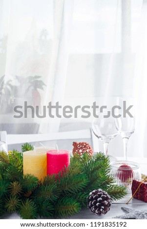 Christmas wreath with colorful big candles on a table with a Christmas table setting on a white wooden table in front of a light window
