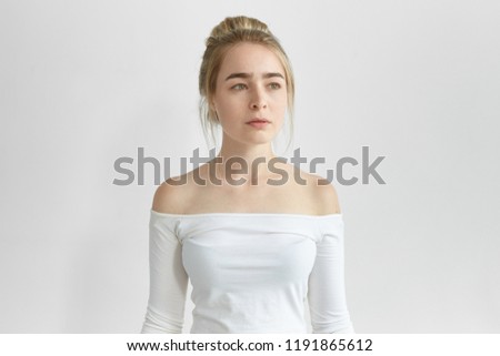 Isolated picture of beautiful young woman with green eyes, smooth skin andhair bun posing against blank white studio wall background, having calm and peaceful facial expression, looking away