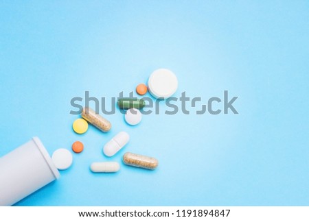 Multi-colored tablets and capsules, white bottle for tablets, pharmaceutical medicine pills on blue background, analgesic against diseases Royalty-Free Stock Photo #1191894847
