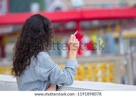 A young woman smoking a cigarette. /  Female hand with smoking cigarette in public area blurred  background. Royalty-Free Stock Photo #1191898078