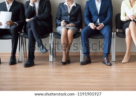Legs of diverse job applicants sitting on office chairs in corridor waiting in turn for interview, feet of work candidates expect in queue for hiring or employment talk. Recruitment concept Royalty-Free Stock Photo #1191901927