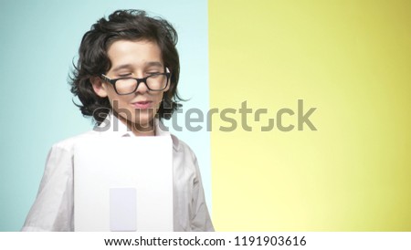 Portraits of a teenager in school uniform and glasses on a colored background. Funny guy. concept of learning. A teenager is holding a laptop, looking at the camera, smiling and making funny faces