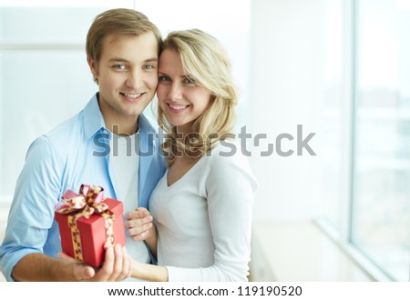 Image of young guy and his girlfriend with giftbox looking at camera