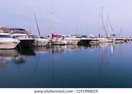 Long exposure picture from sportive harbour with line of boats and your reflections in the blue calm water at the end of the day in mediterraean see at spain