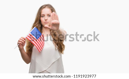 Young blonde woman holding flag of USA with open hand doing stop sign with serious and confident expression, defense gesture