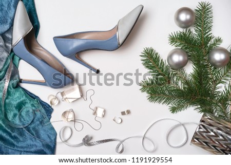 Flat lay female stylish accessories fashion outfit: blue cloth, shoes earrings necklace silver ribbon branches fir tree white background. Christmas Happy New Year Party conception. copy space