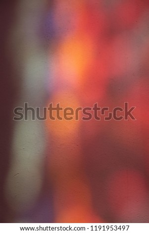 Blur colorful reflects of stained glass on a wall church. Abstract design with many colors as pink, purple, orange and blue. Textured lighted surface with bokehs. Blurred artistic shapes.  