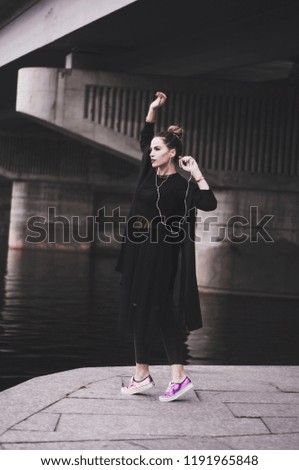 Fashionable brunette girl in black clothes with headphones listening to music. In movement. Black style.