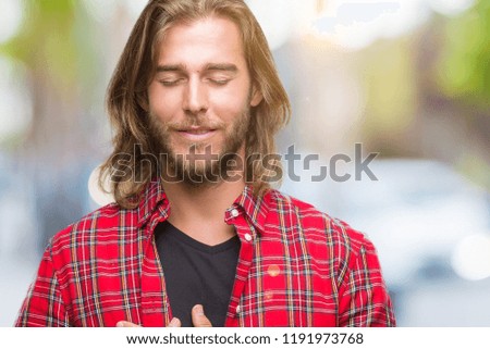 Young handsome man with long hair over isolated background smiling with hands on chest with closed eyes and grateful gesture on face. Health concept.