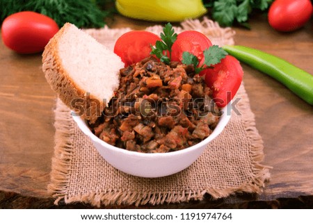 A portion of vegetable stew with eggplant, a piece of white bread with tomato slices and parsley in a white bowl.