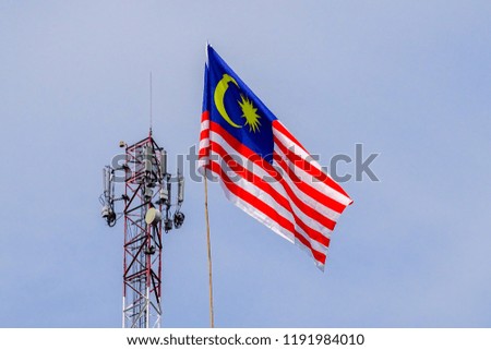 Malaysian Flags or Jalur Gemilang with telecomunication tower against blue sky.