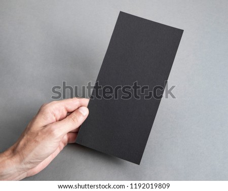 Mens hand holding empty black flyer on light gray background. Blank paper mock-up