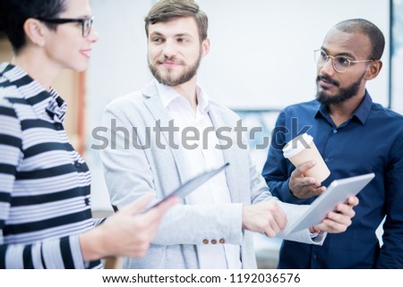 Confident team planning new project: content enterprising bearded male manager using tablet while presenting his idea to colleagues in lobby