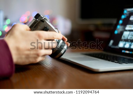 young male photographer holding a camera and prcessing his photos on laptop in the studio