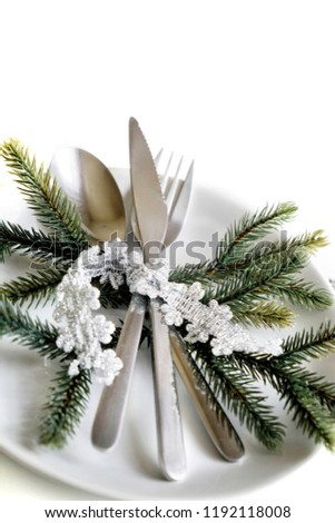 Picture of Christmastime table setting, white festive plate with knife and fork, shiny silver decoration, candle light, home interior, beautiful holiday dinnerware, romantic New Year dinner