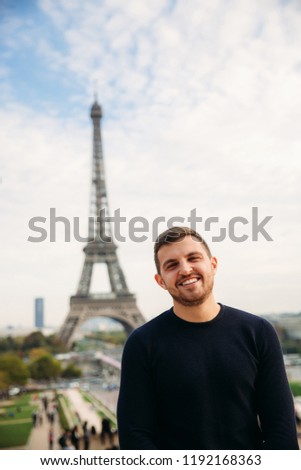 Cheerful man tourist in dark blue pullover is standing on the background of the Eiffel Tower