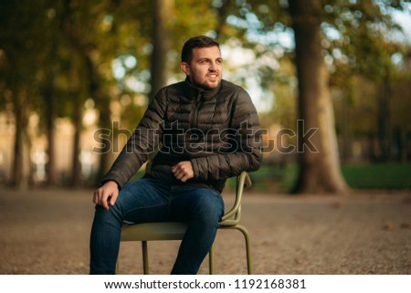 Handsome man sits in the middle of the park in khaki stool
