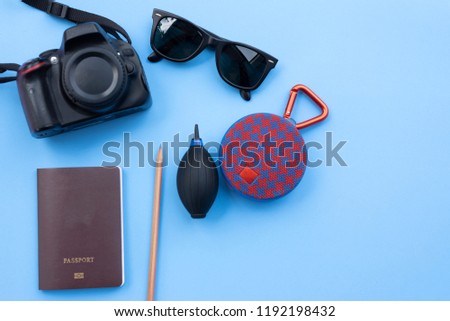 DSLR camera sunglasses passport pencil camera’s blow and Bluetooth speaker on blue pastel background. This accessories for travel out countries