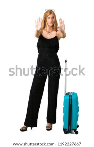 Blond girl traveling with her suitcase making stop gesture with her hand denying a situation that thinks wrong on isolated white background