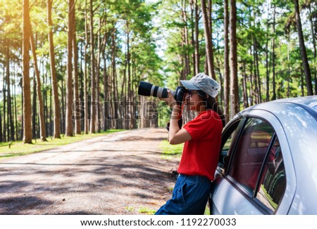 Young asian woman travels by car take a photograph in pine forest.