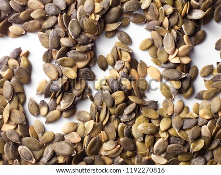 Dried raw pumpkin seeds arranged in a pattern and photographed on a white background