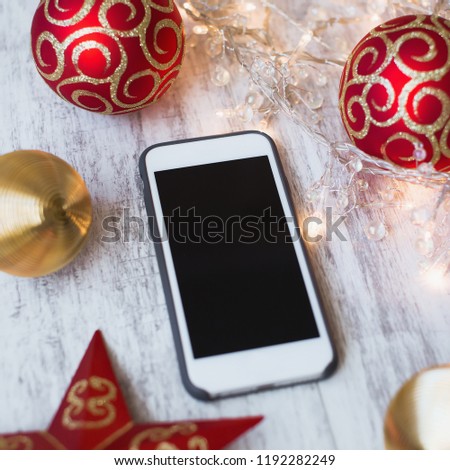 Smartphone on a white wooden background with christmas toys and lights