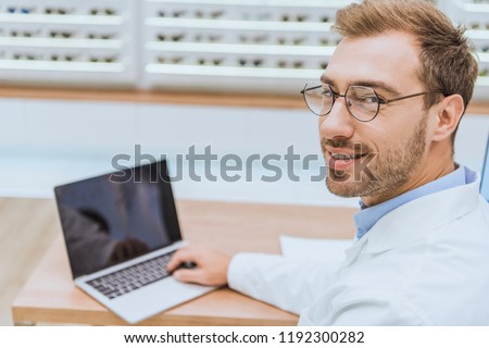 professional handsome optometrist using laptop in ophthalmic shop Royalty-Free Stock Photo #1192300282