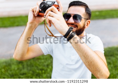 Stylish hipster with a camera, taking pictures, walking around the city in a good mood