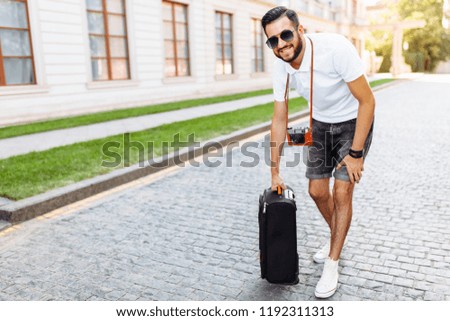 Young hipster male hiker with beard, walks around town with a suitcase and a camera around my neck