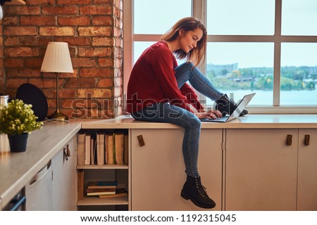 Young beautiful student girl sitting with laptop on window sill in student dormitory. Royalty-Free Stock Photo #1192315045