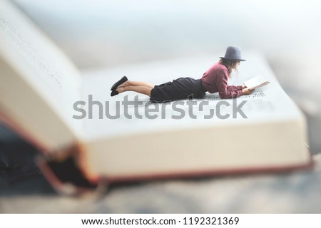 surreal situation of a woman reading her book lying on a giant book