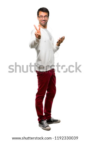 A full-length shot of a Man with glasses and listening music smiling and showing victory sign on white background