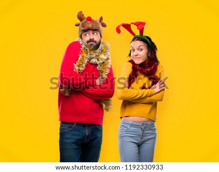 Couple dressed up for the christmas holidays making unimportant gesture while lifting the shoulders on yellow background