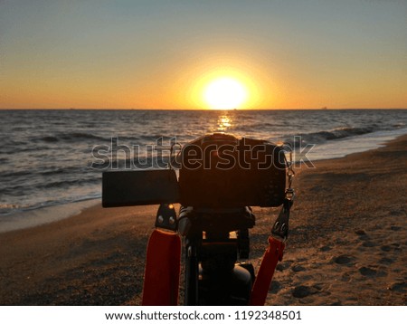 Camera with tripod on seashore during sunrise