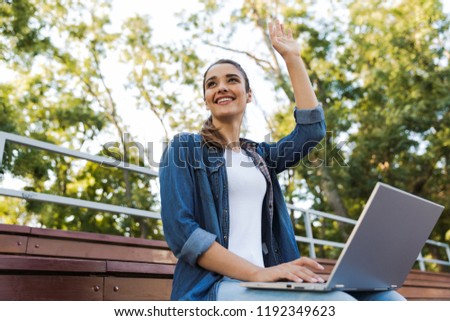 Image of amazing young beautiful woman sitting outdoors using laptop computer waving.